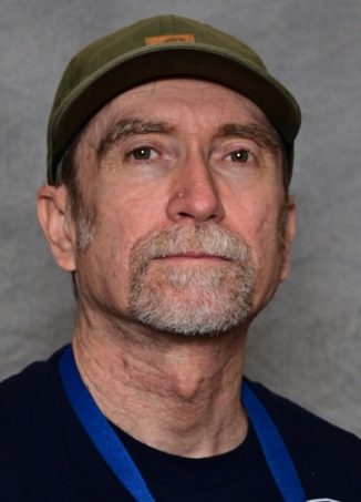 Man wearing olive cap and blue lanyard against gray background.
