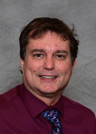 Professional headshot of man in maroon shirt and patterned tie.