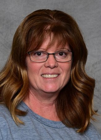 Woman with brown wavy hair wearing glasses smiling.