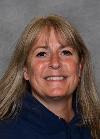 Smiling woman with long brown hair wearing dark blue jacket.