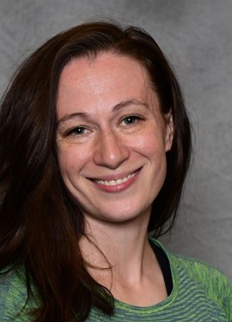 Woman with long dark hair wearing green striped shirt smiling