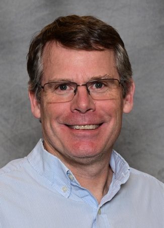 Man wearing glasses and light blue striped shirt smiling.