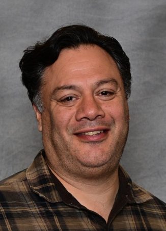 Professional headshot of smiling man in plaid shirt.