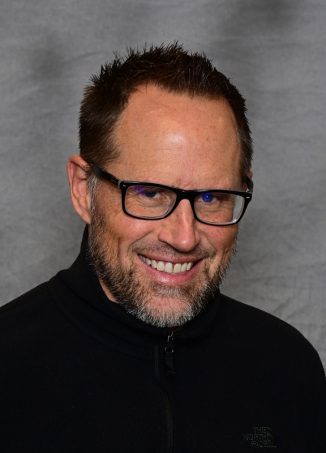 Man wearing glasses and black jacket smiling at camera