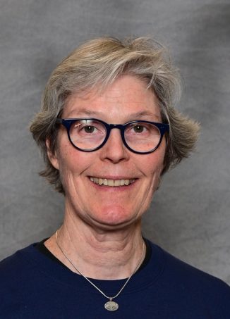 Woman with gray hair, glasses, wearing dark blue shirt and pendant necklace.