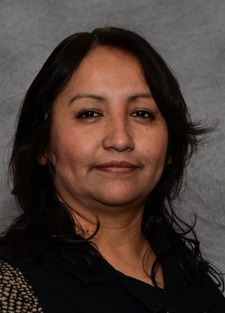 Professional headshot of woman with long black hair against gray background.