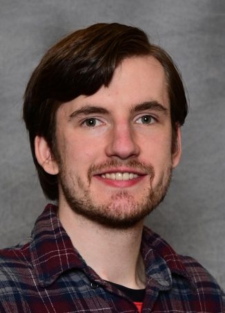 Smiling man with brown hair wearing plaid shirt.