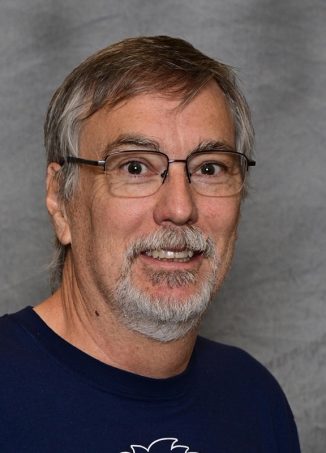 Man wearing glasses and dark blue shirt, smiling at camera.