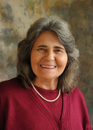 Professional portrait of woman with gray hair wearing burgundy sweater.