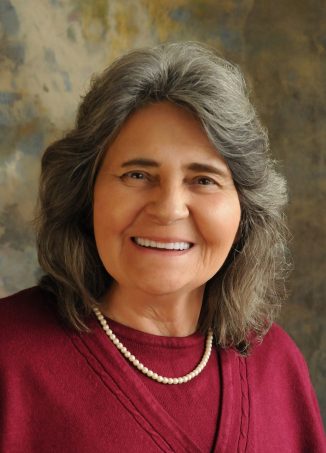 Woman with gray hair wearing burgundy sweater and pearl necklace smiling