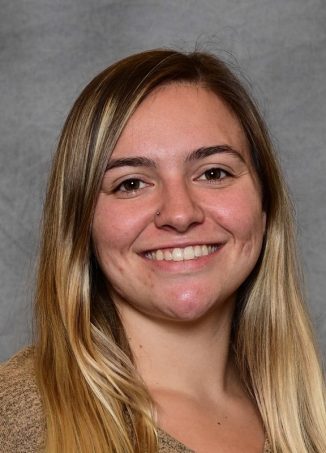 Portrait of smiling woman with brown hair against gray background.