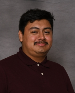 Professional headshot of a man with dark hair and mustache wearing maroon shirt.