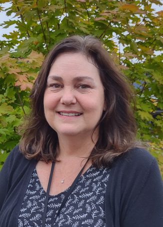 Woman smiling outdoors with autumn foliage background.
