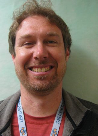 Man wearing red shirt and lanyard smiling at camera.