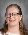 Woman with glasses and long brown hair smiling at camera.
