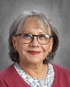 Woman with gray hair and glasses wearing maroon and white collar.