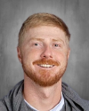 Smiling man with red beard wearing gray shirt, portrait photo.