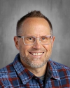 Smiling man with glasses wearing blue plaid shirt.
