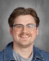 Man wearing glasses and blue shirt, smiling at camera.
